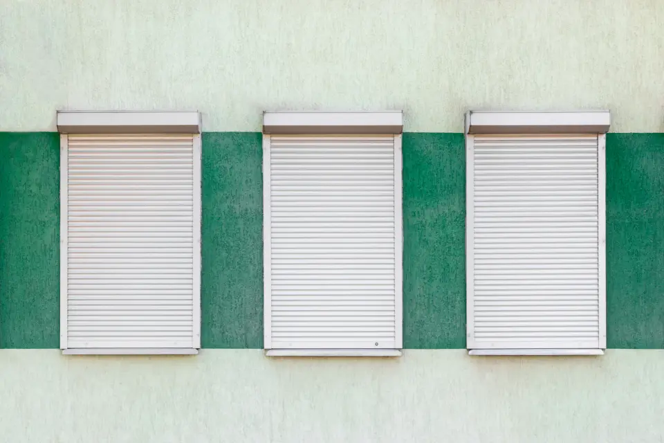 Drie witte rolluiken, half neergelaten, in een groene gevel