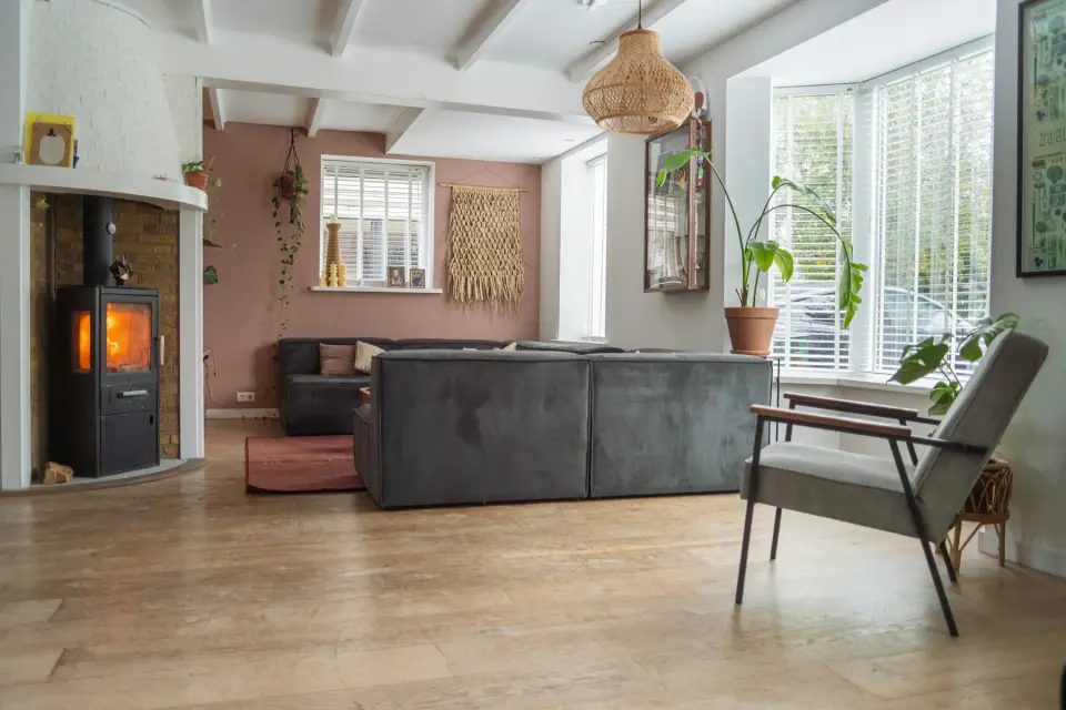 Lichte woonkamer met een houtlookvloer, een grijze bank en een houtkachel